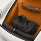 Black leather duffel bag and suitcase in a car trunk with brown interior.