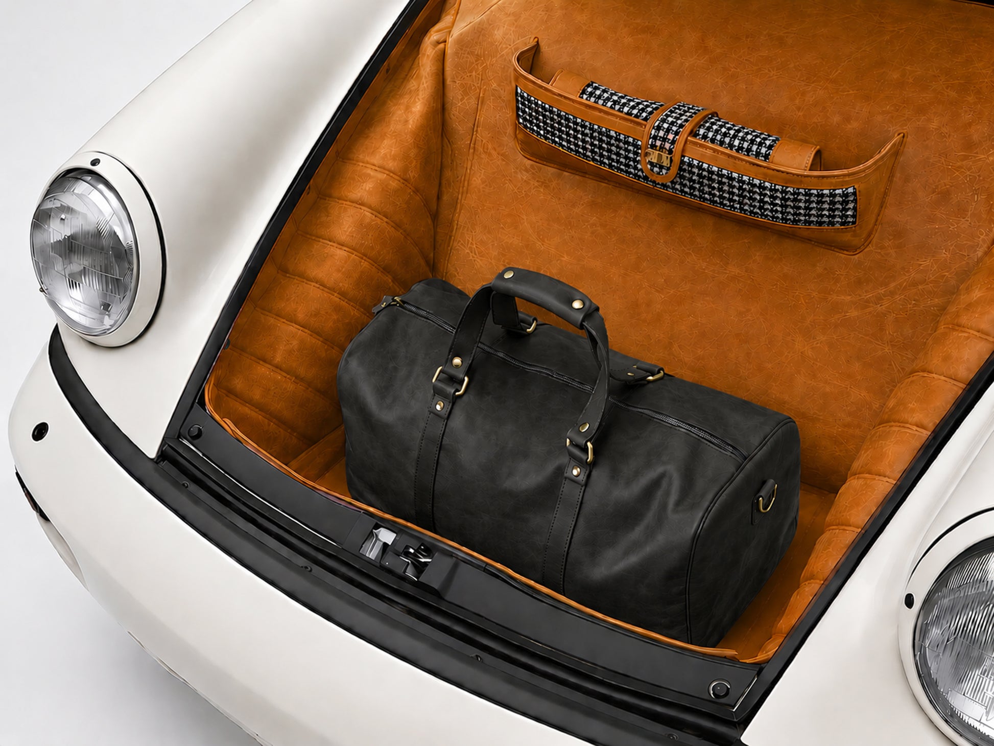 Black leather duffel bag and suitcase in a car trunk with brown interior.