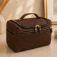 Brown leather toiletry bag with gold zippers on a beige surface.