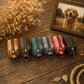 Six small zippered pouches in assorted colors are arranged in a row on a rustic wooden surface, with dried flowers, rope, and a framed dog photo in the background.