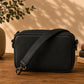 Black leather crossbody bag on a wooden surface with books and a plant in the background