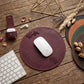 A round burgundy leather mouse pad with 'Wendy' and a monogram logo, styled on a rustic wooden desk with a white mouse, keyboard, earbuds case, and other desk accessories.