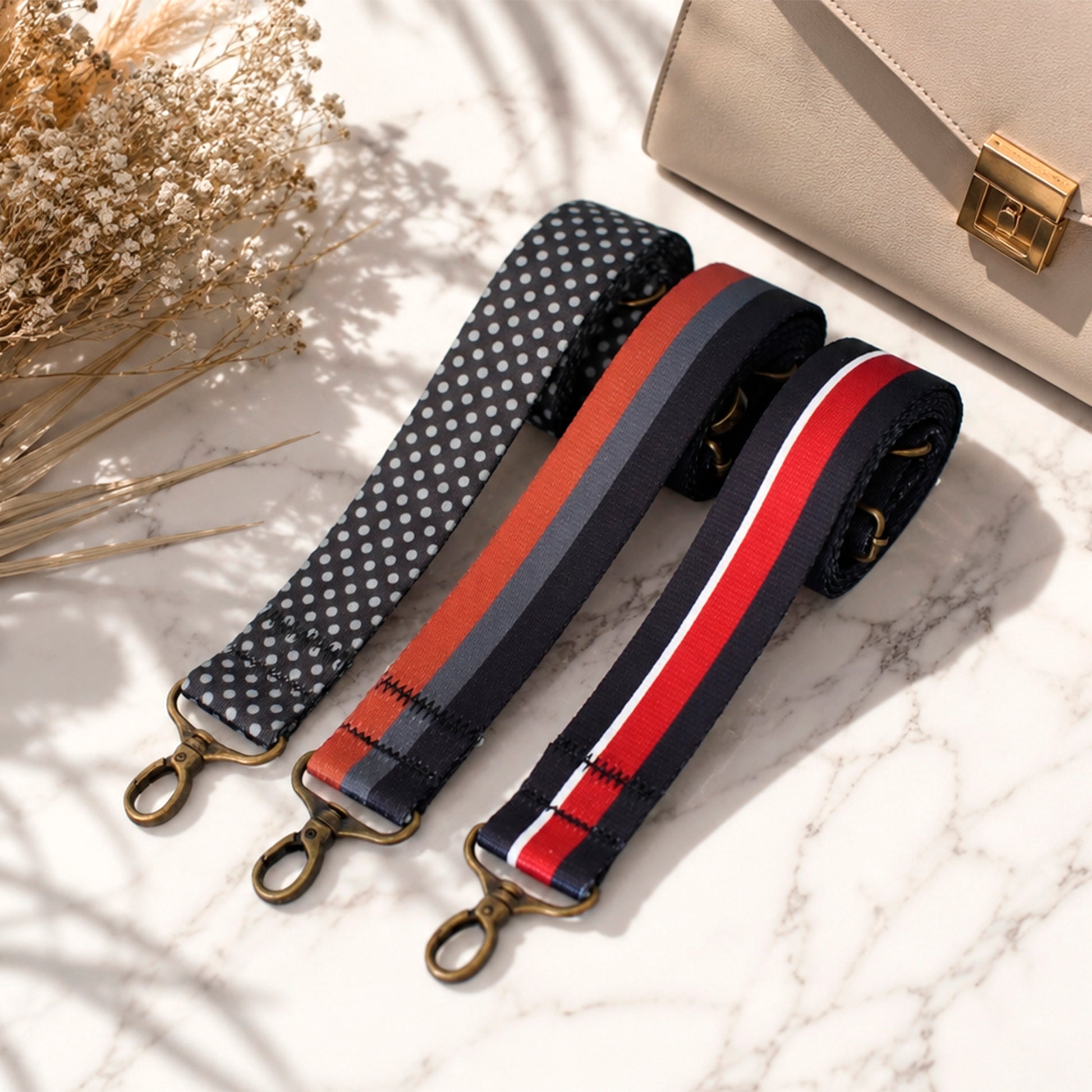 Three colorful bag straps on a marble surface with a beige handbag.