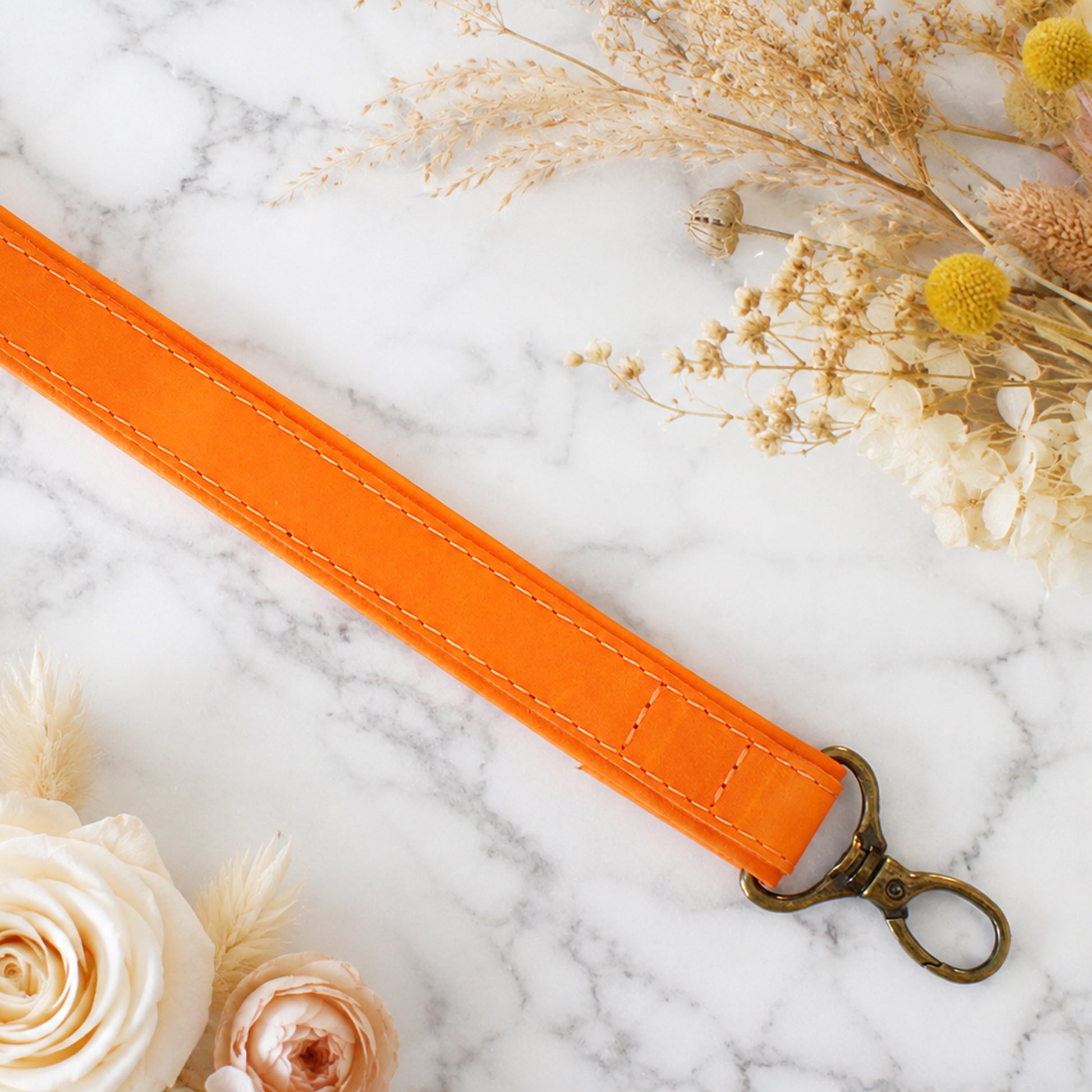 Orange strap with a gold clasp on a marble surface with flowers