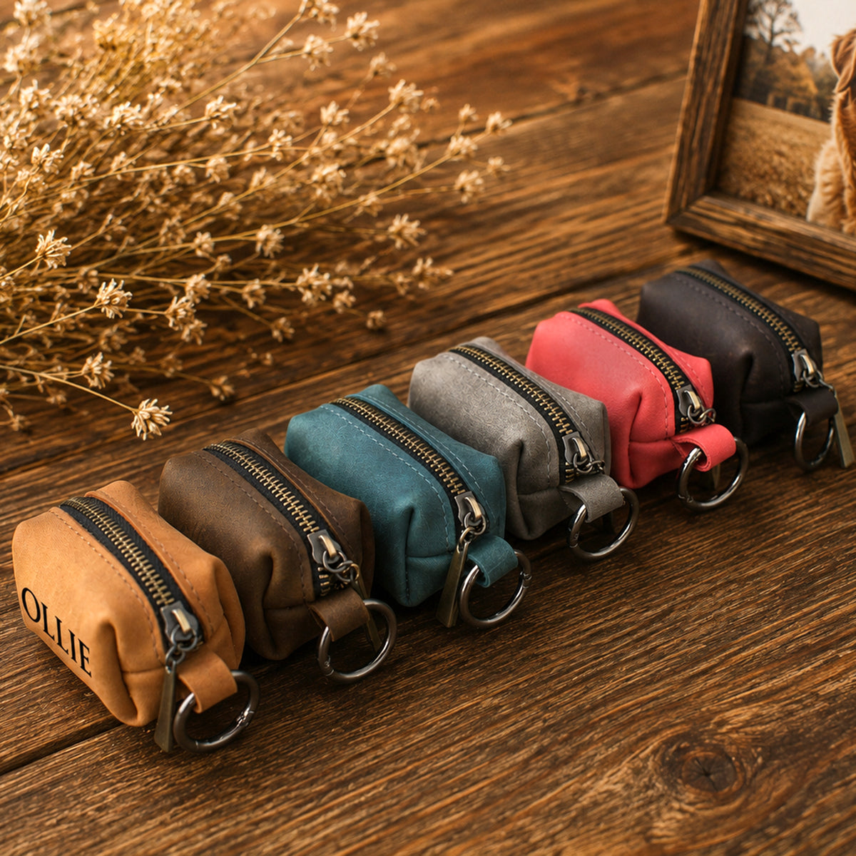 Six small zippered pouches in assorted colors are arranged in a row on a wooden surface. The pouches include tan, brown, teal, gray, pink, and black, each with a metal key ring and zipper.