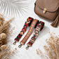 Two patterned bag straps with a brown leather bag on a light surface with dried plants.