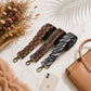 Three patterned bag straps on a marble surface with a phone and handbag.