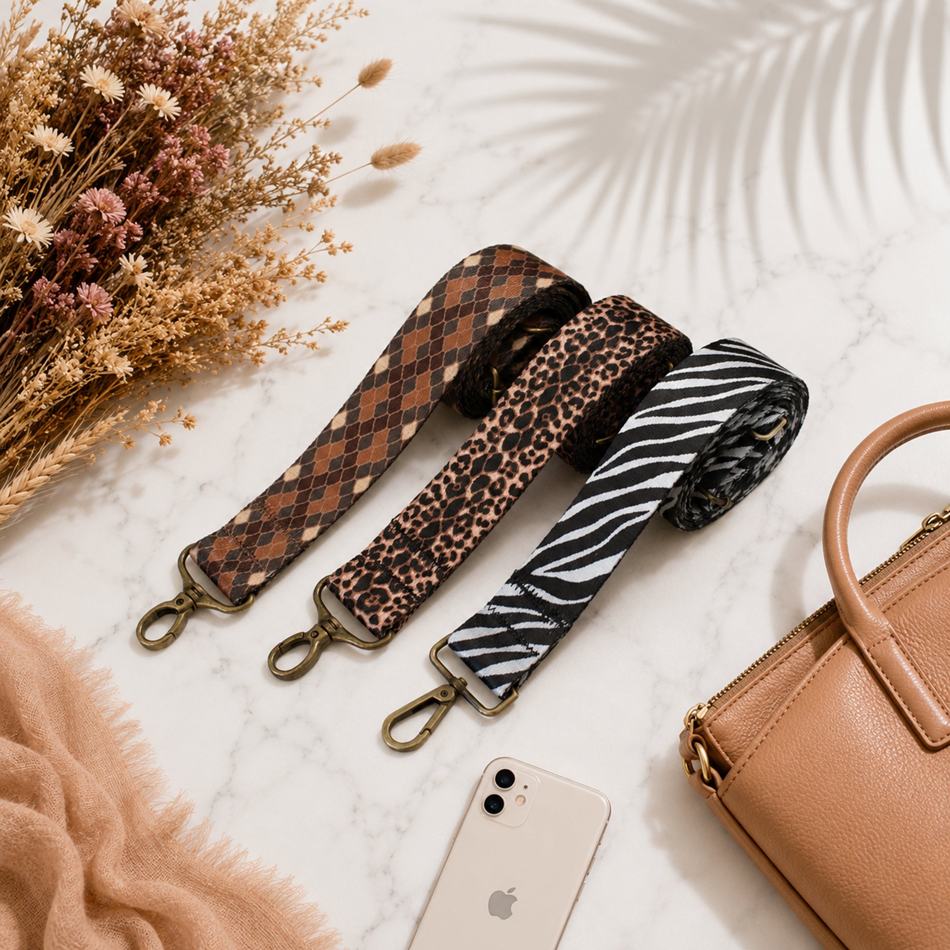 Three patterned bag straps on a marble surface with a phone and handbag.