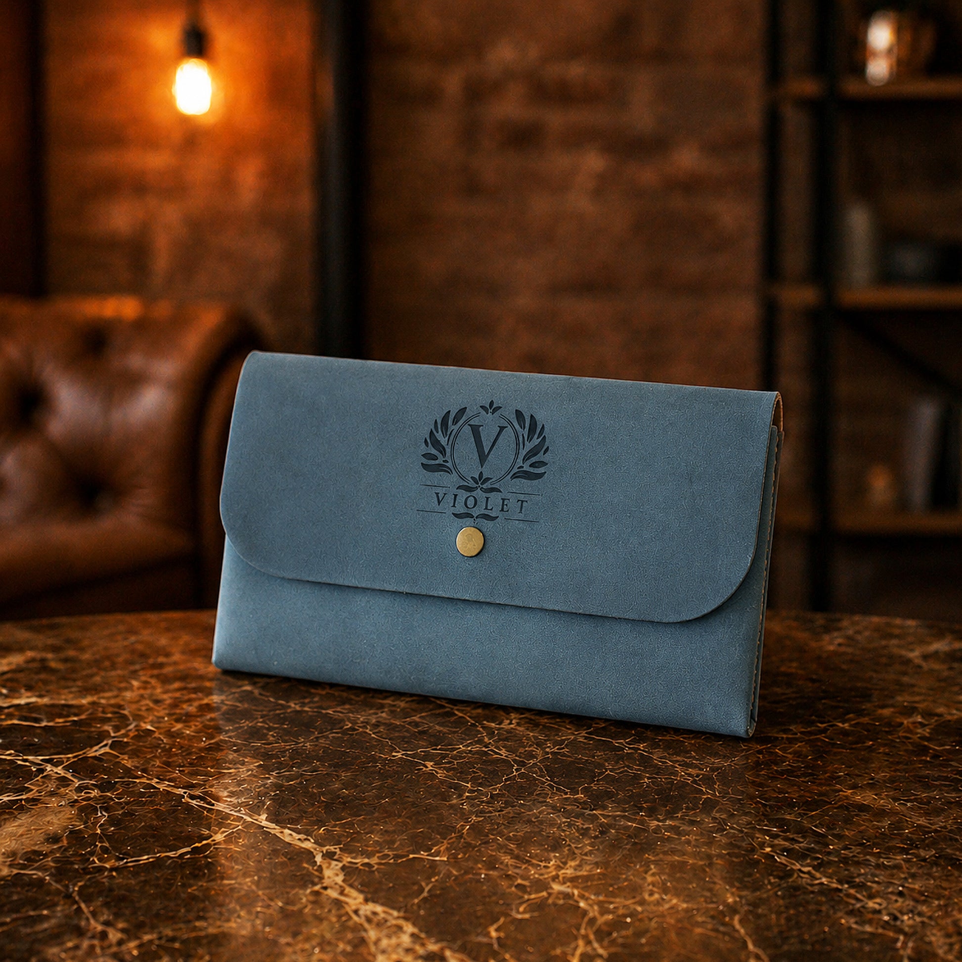 Blue leather clutch with a brand logo on a marble surface with a warm-toned background.