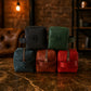 Five leather bags in black, green, brown, and red with monogram initials on a marble surface.