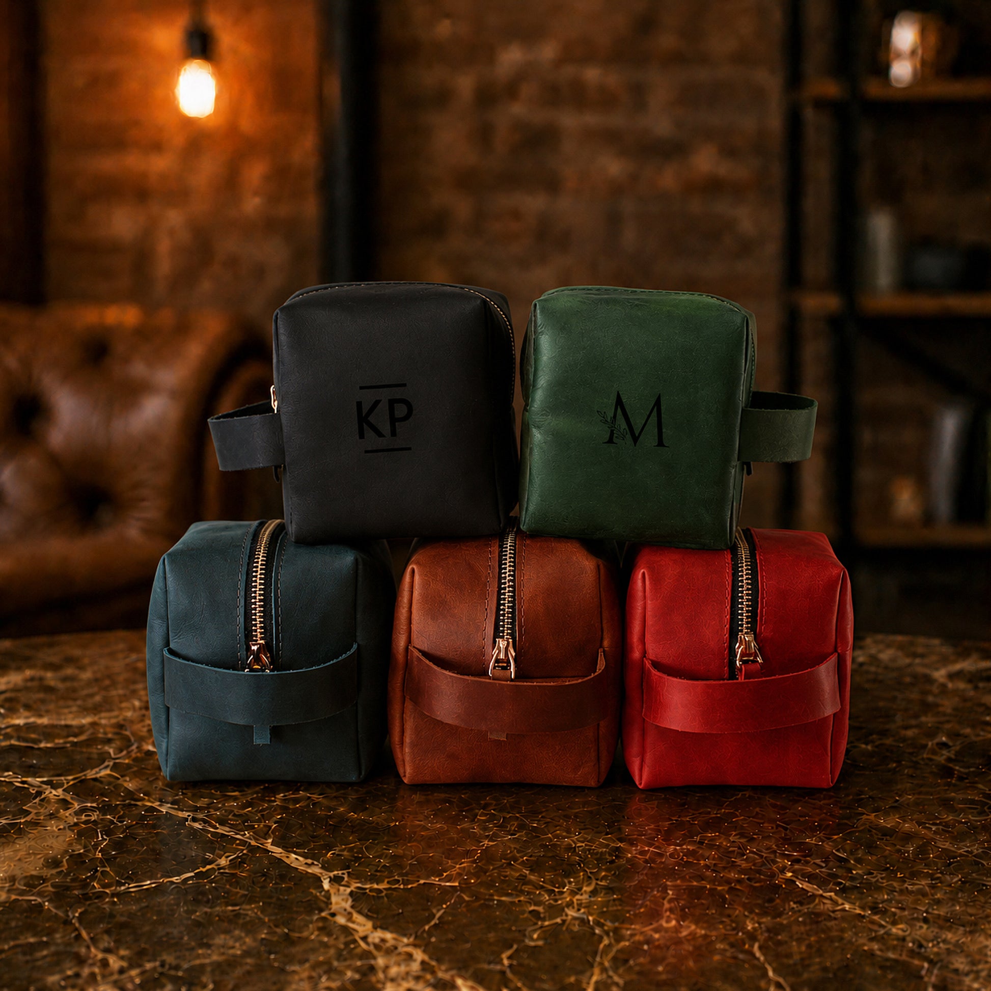 Five leather bags in black, green, brown, and red with monogram initials on a marble surface.