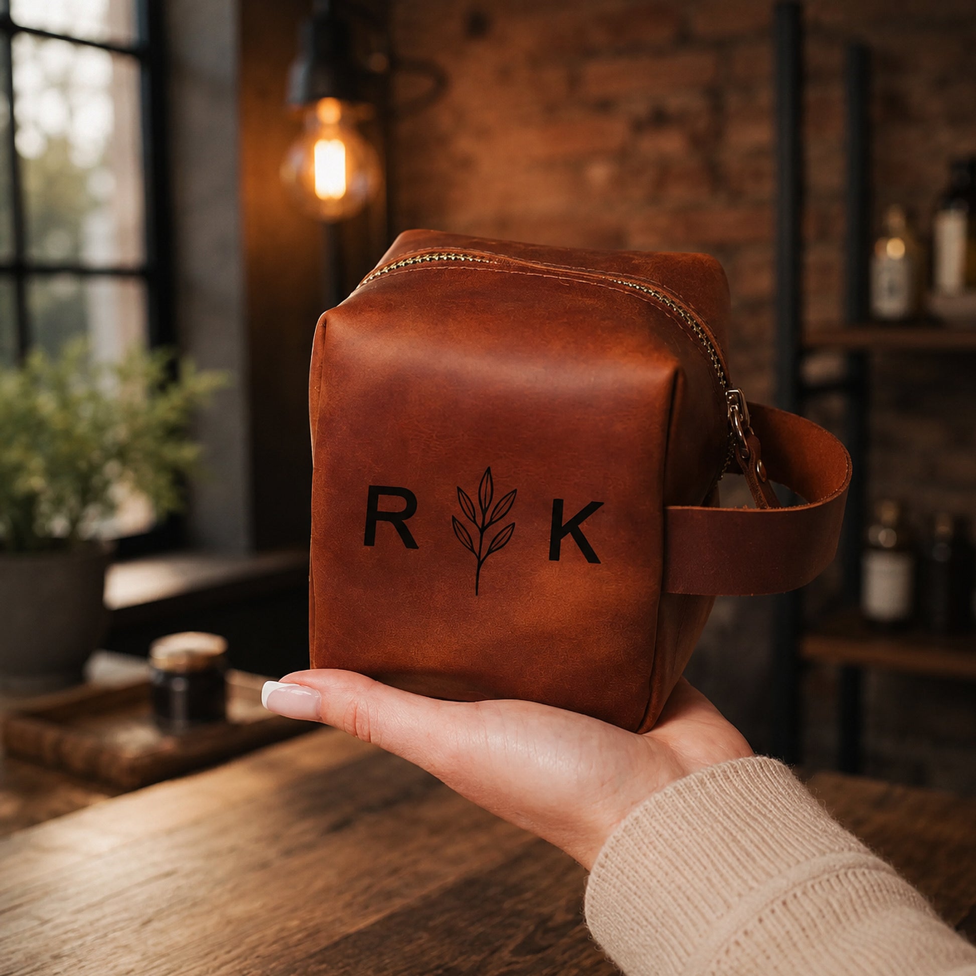 Brown leather pouch with 'R K' branding held in a hand against a rustic background