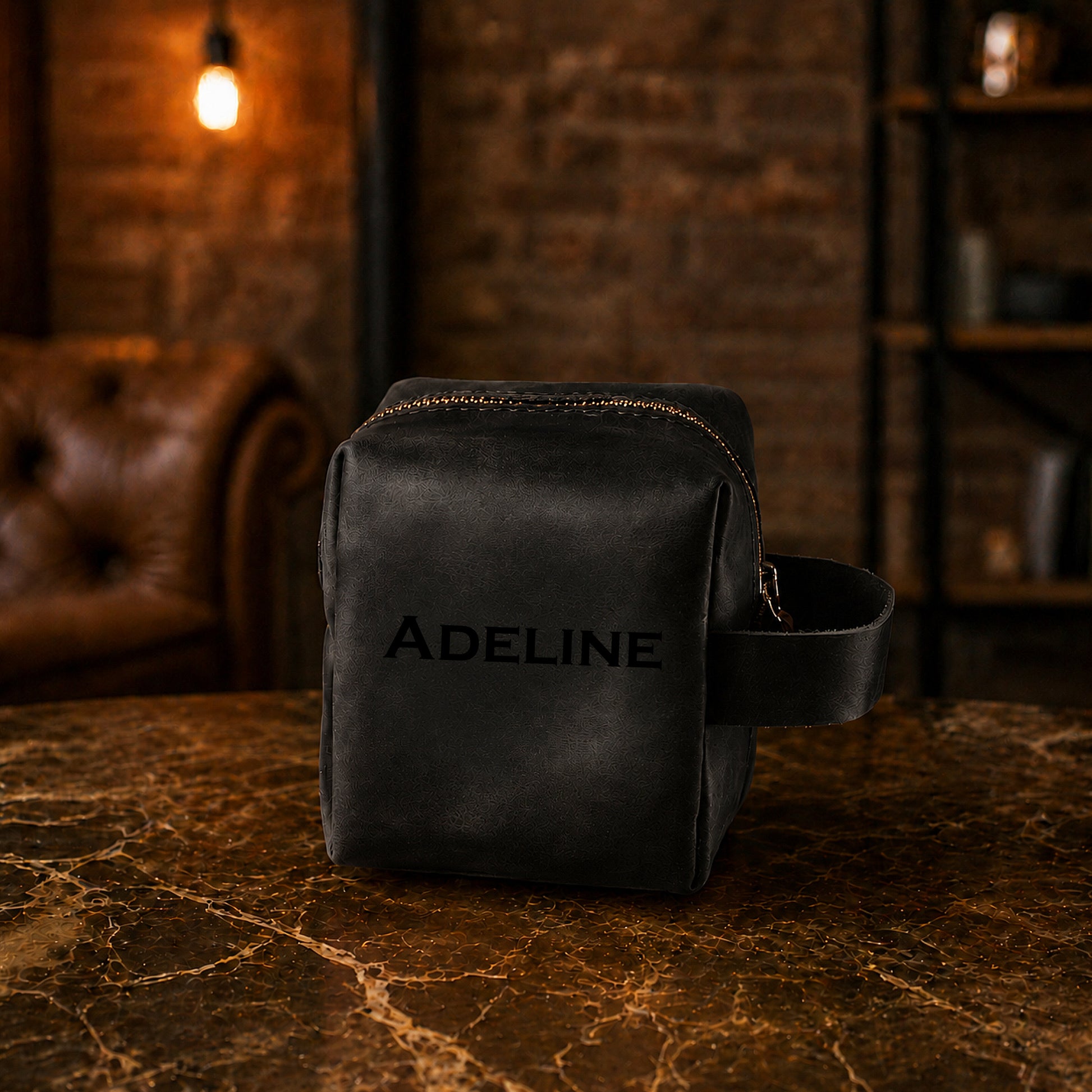 Black leather bag with 'Adeline' branding on a textured surface with a warm-toned background.