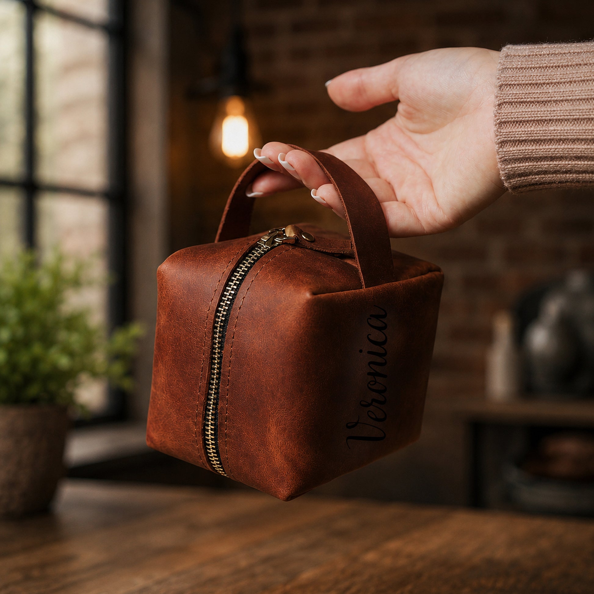 Brown leather bag with 'Veronica' branding held by a hand in a warm-toned indoor setting.