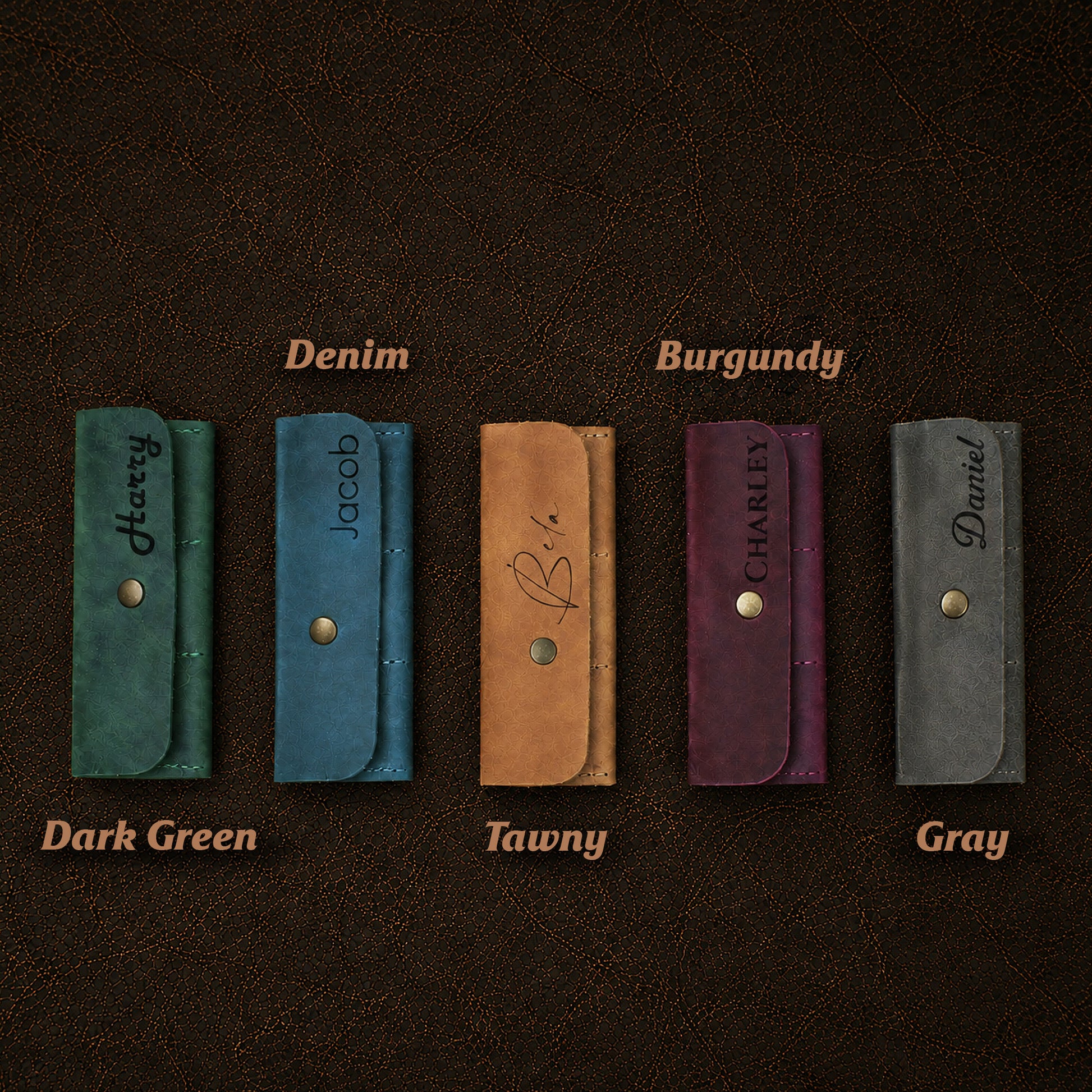 Five leather wallets in different colors with names engraved on a dark brown background.