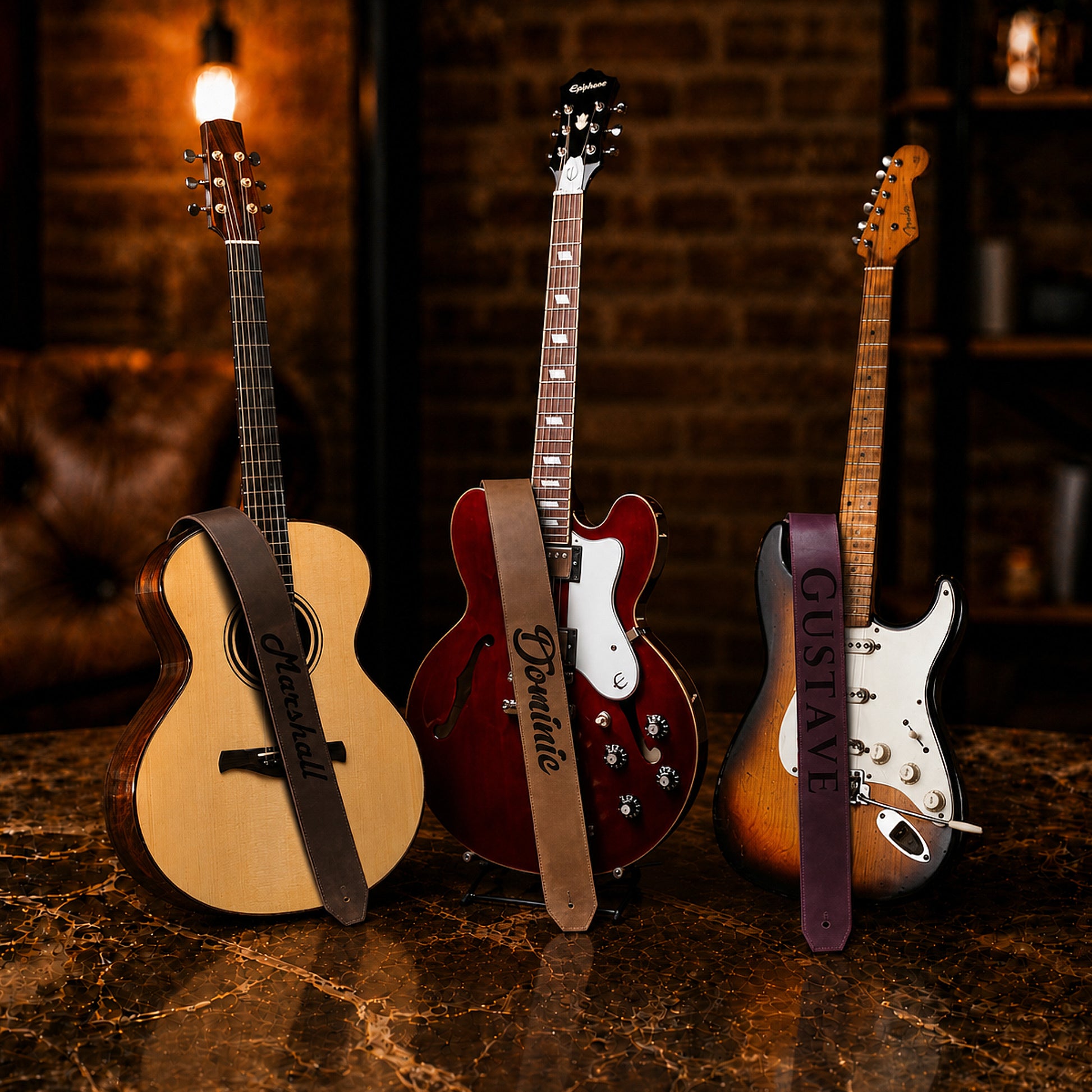Three guitars with branded straps on a dark surface against a brick wall.