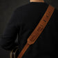 Person wearing a brown guitar strap over a black shirt on a dark background