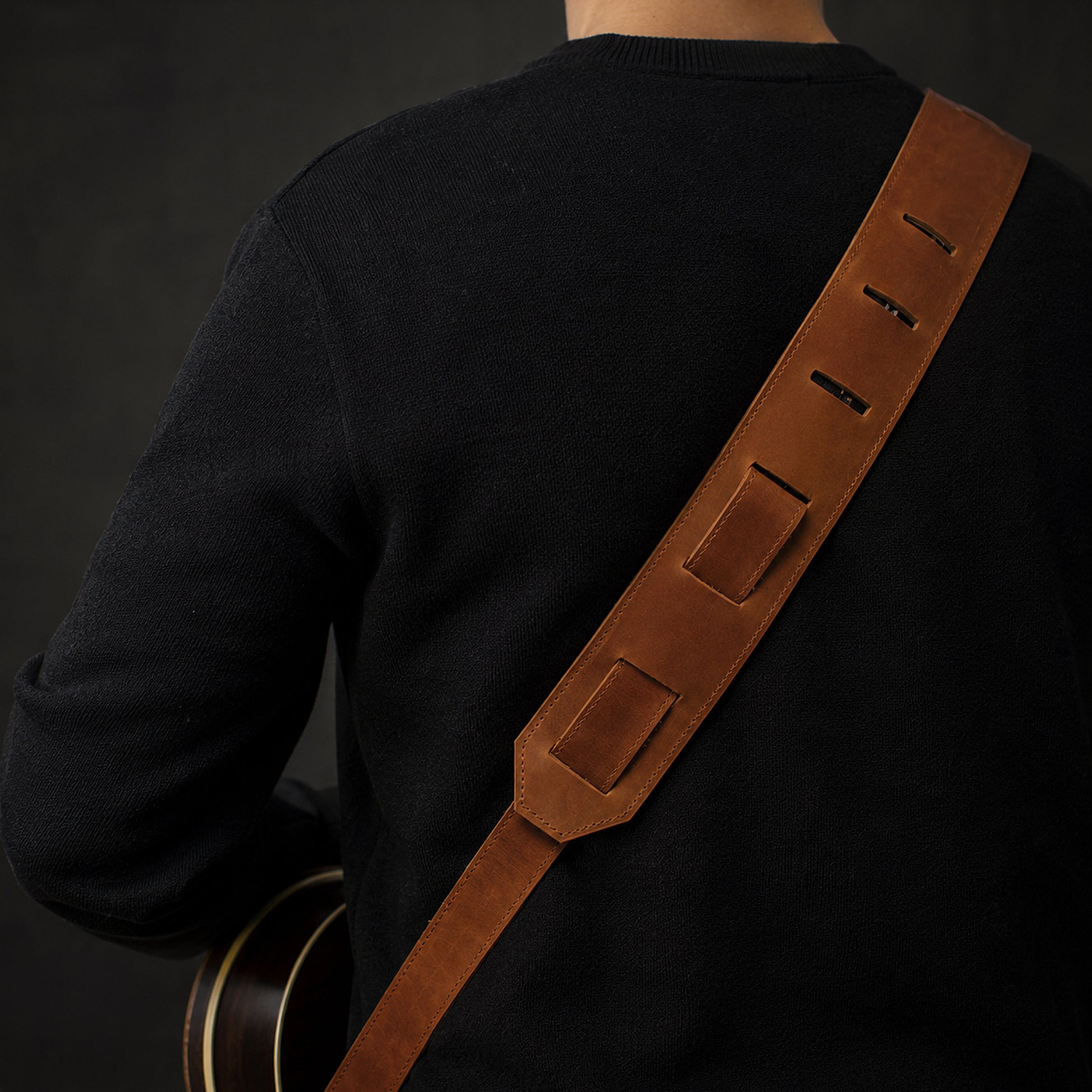 Person wearing a brown guitar strap over a black shirt on a dark background