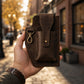 Hand holding a brown leather wallet on a city street