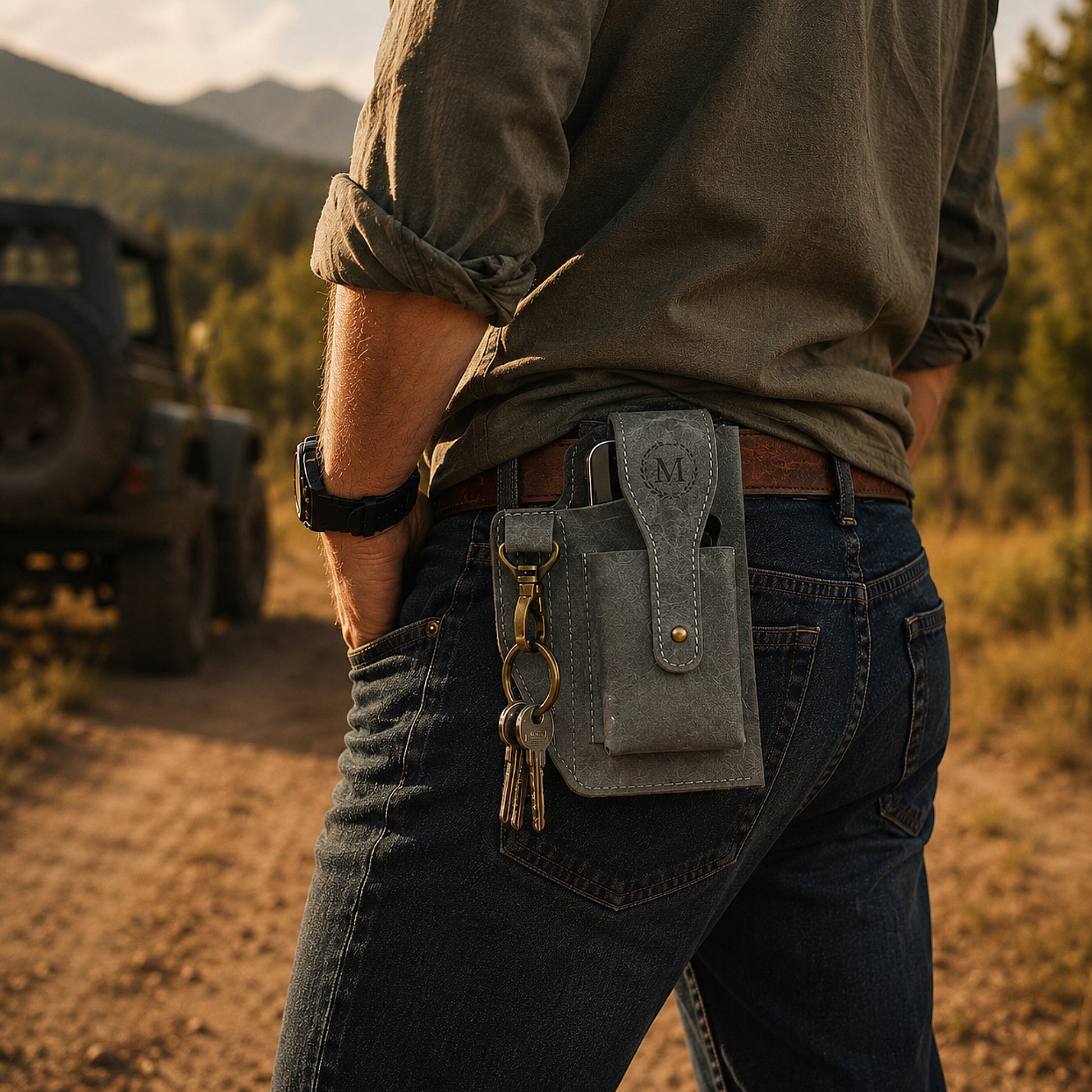 Person wearing a gray utility belt with a pouch and keys, standing in a natural outdoor setting with a jeep in the background.