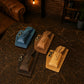 Four leather pouches in blue, brown, and beige on a textured surface with a warm-toned background.