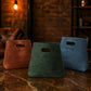 Three leather bags labeled 'Ashley', 'SK1', and 'Tiffany' on a marble surface with a warm-toned background.