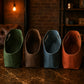 Four fabric bags in green, brown, blue, and orange on a textured surface with a warm light in the background.