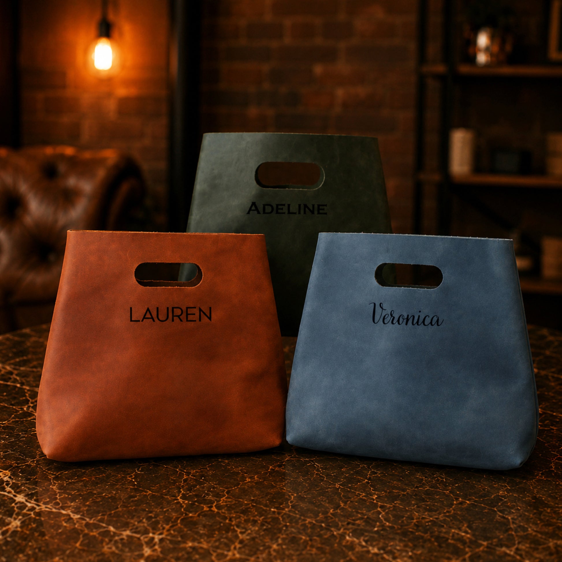 Three bags with names embossed on them, placed on a textured surface with a warm-toned background.