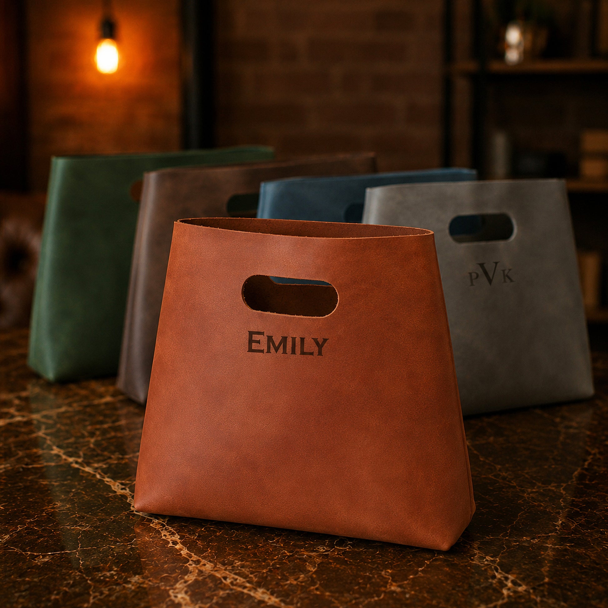Brown leather bag with 'EMILY' engraved, surrounded by other bags on a dark surface.