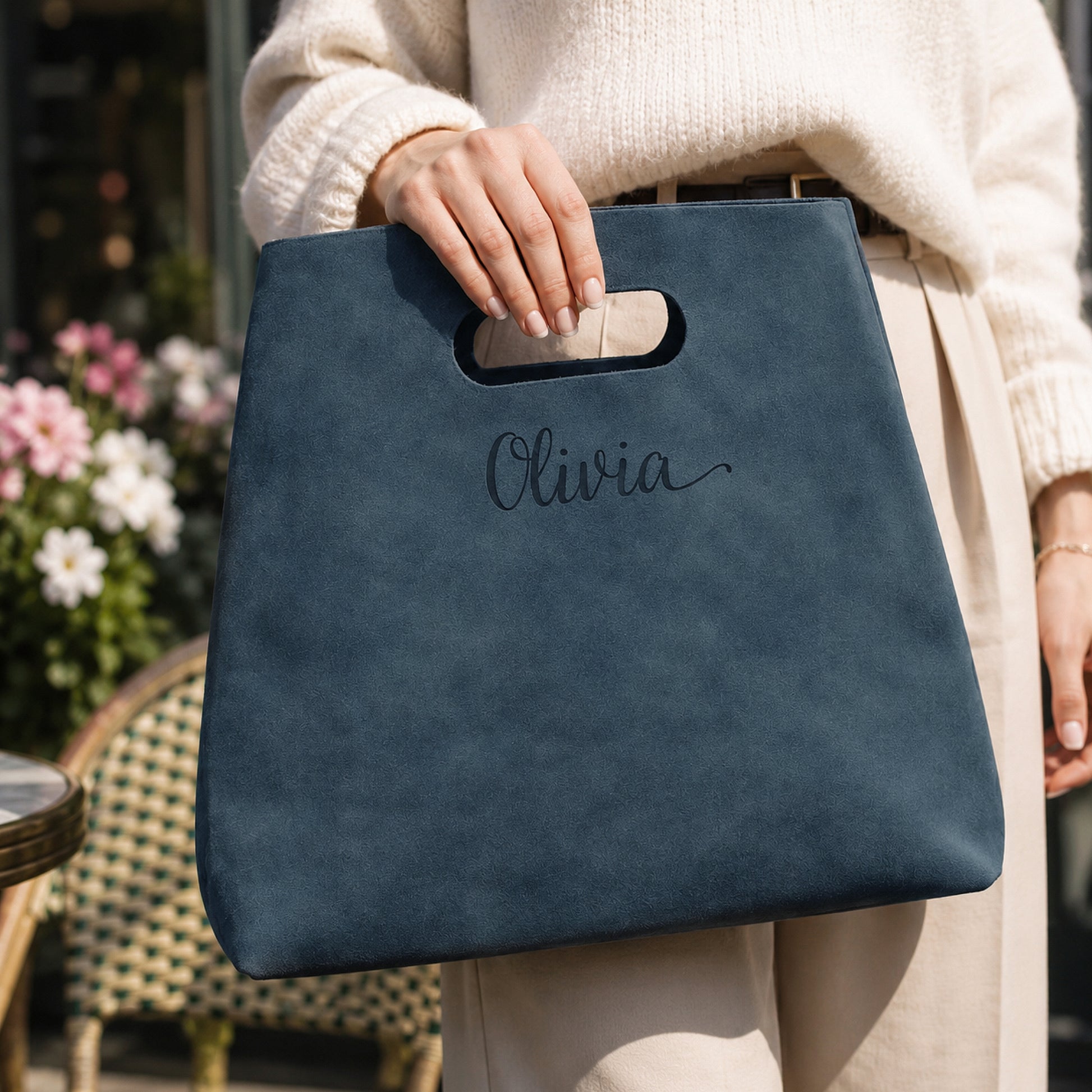 Person holding a blue bag with 'Olivia' embroidered on it, outdoor setting.