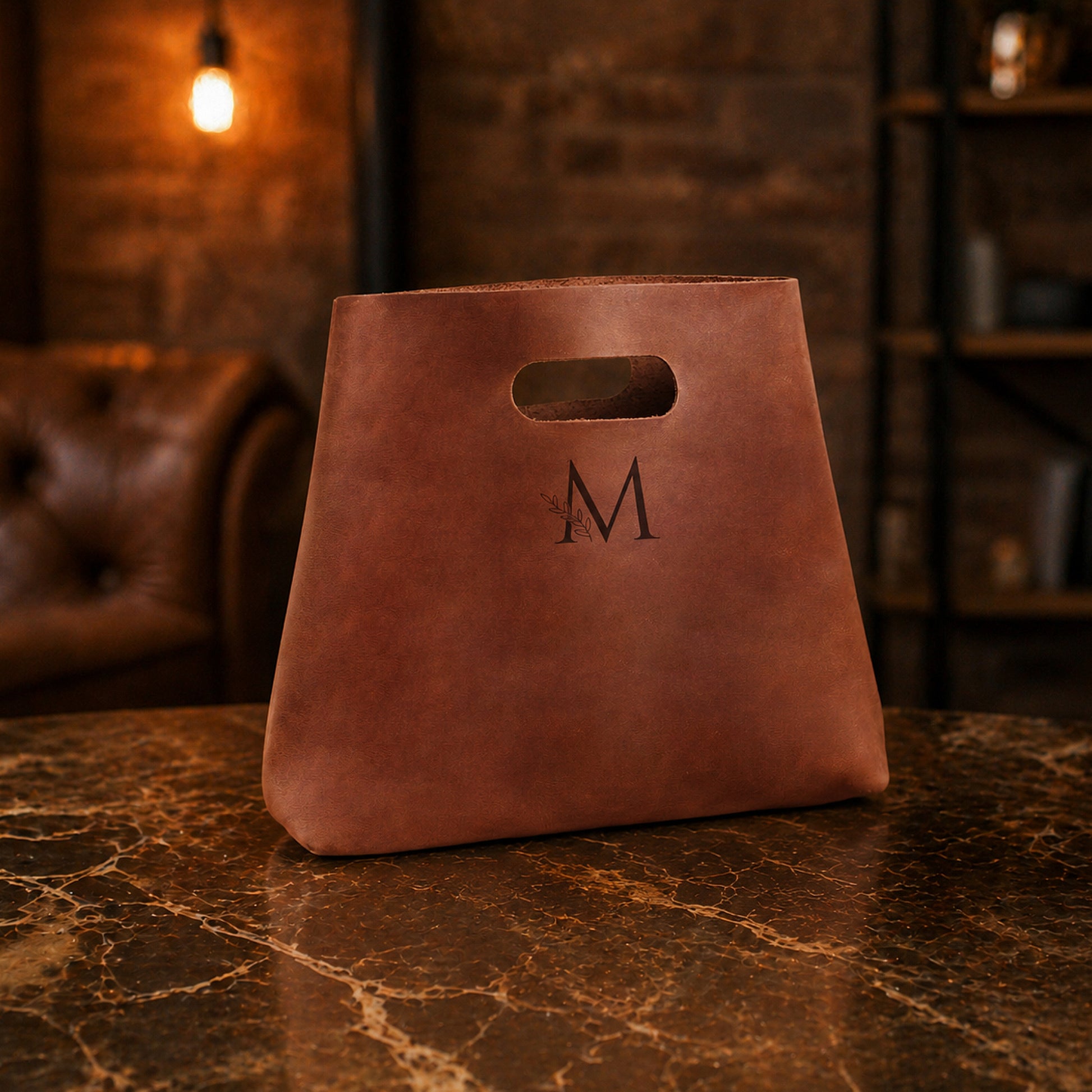 Brown leather bag with a monogram 'M' on a marble surface with a blurred background