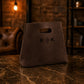 Brown leather bag with 'R K' logo on a marble surface with a warm, blurred background.