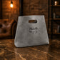Gray bag with 'Michelle' and a leaf design on a marble surface with a warm-toned background.