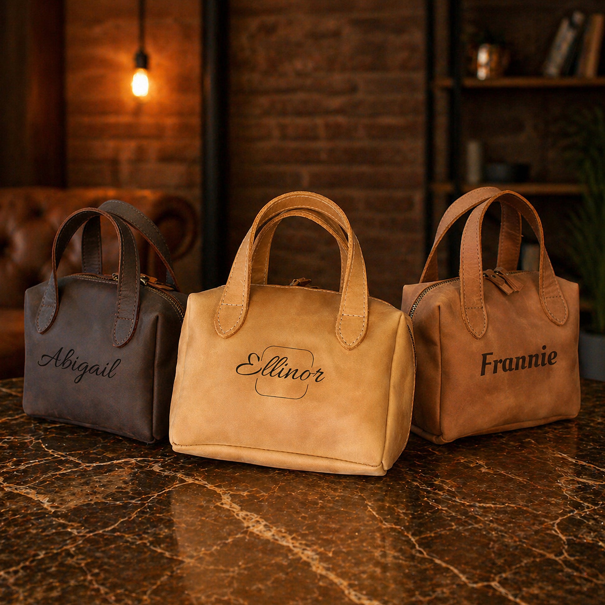 Three leather handbags with names engraved on them, placed on a marble surface.