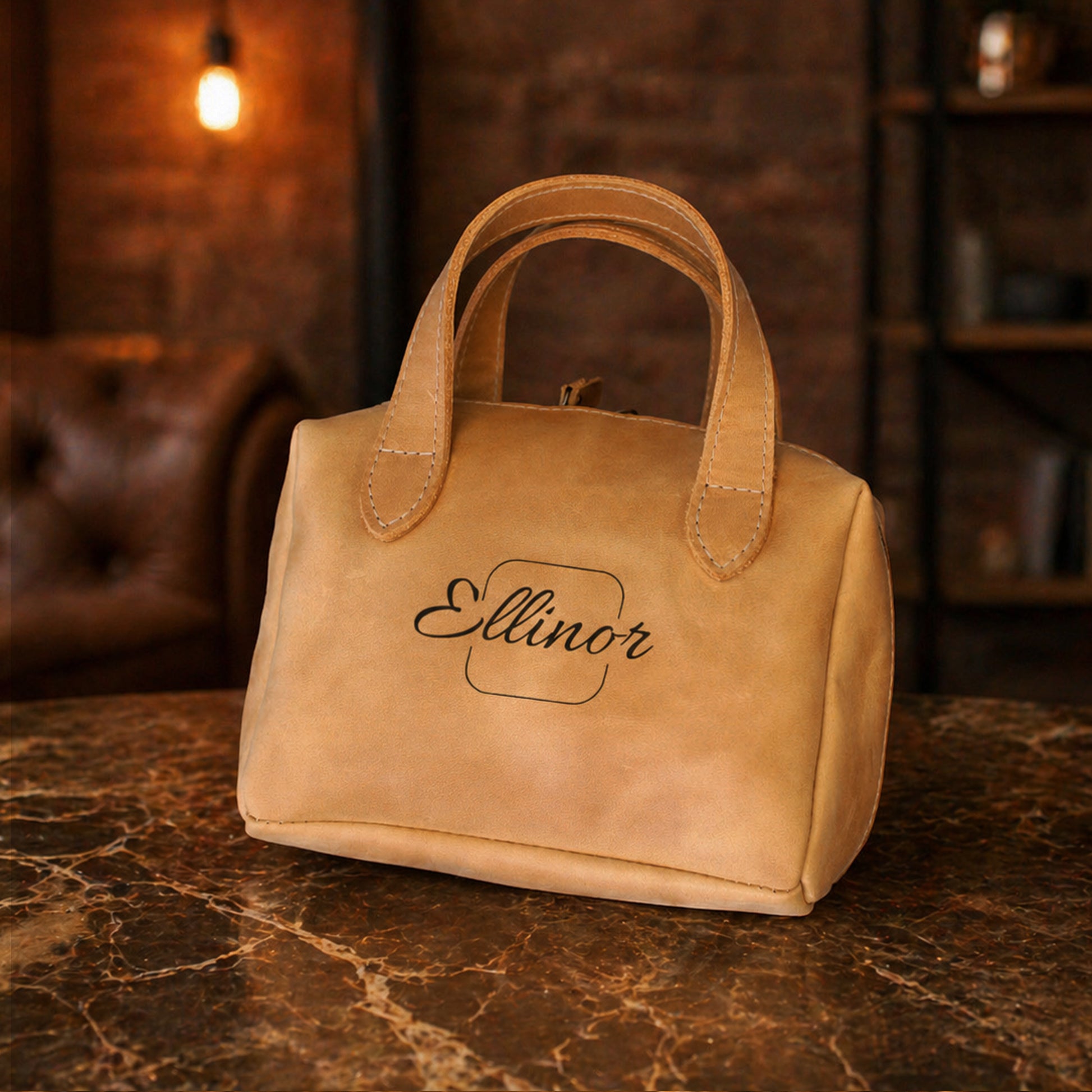Tan leather handbag with 'Ellinor' branding on a marble surface with a dark background.