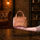 Brown leather handbag with 'BEATRICE' branding held by a person in a warm-toned room.