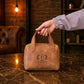 Brown leather bag with 'Darian' logo held by a hand on a marble surface with a warm, rustic background.