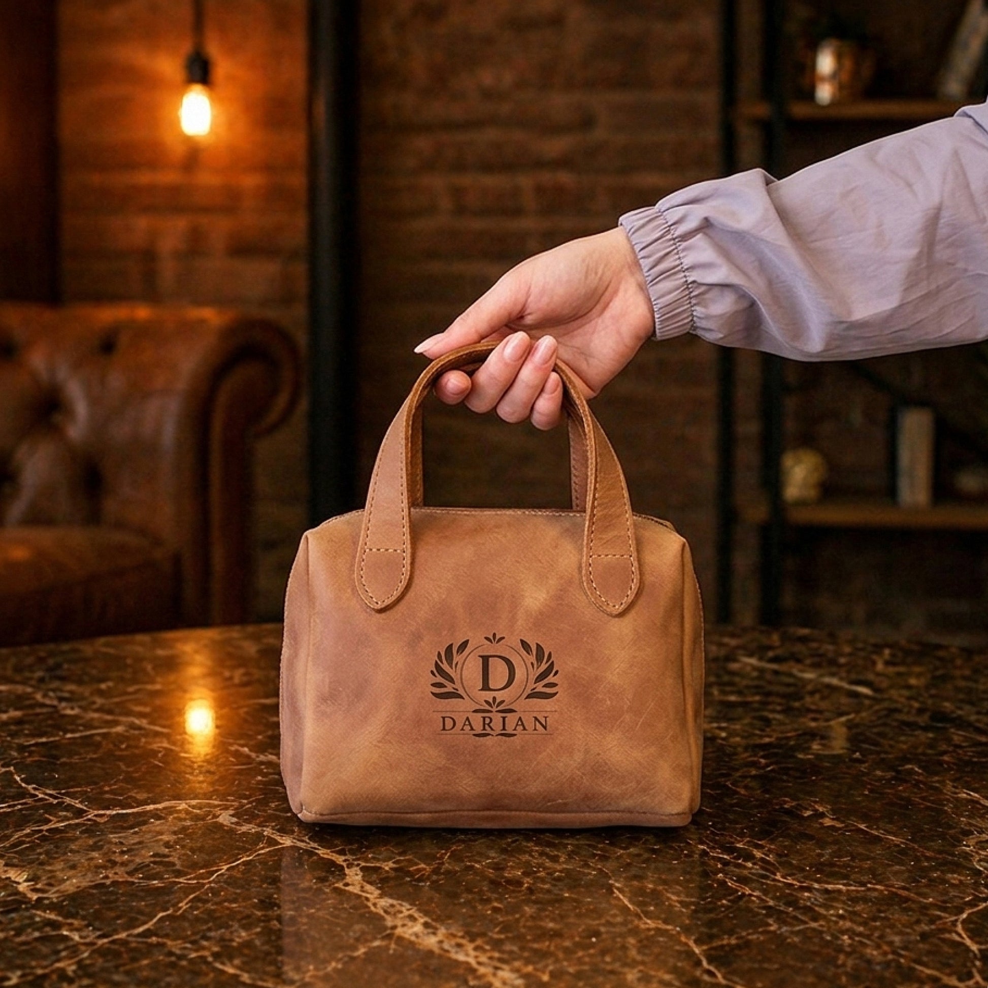 Brown leather bag with 'Darian' logo held by a hand on a marble surface with a warm, rustic background.