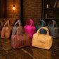 Collection of handbags in various colors on a textured surface with a warm light in the background.