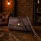 Brown leather handbag with a brand logo on a dark surface with a blurred background