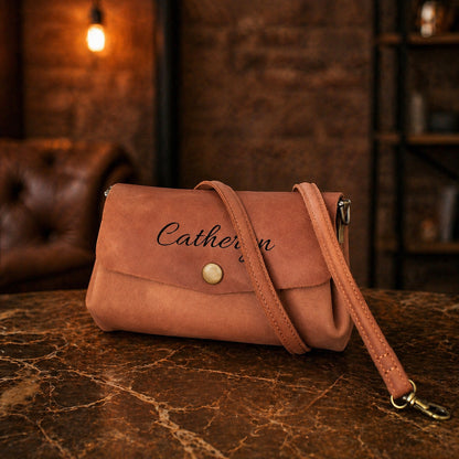 Brown leather handbag with 'Catherine' engraving on a marble surface with a rustic background.